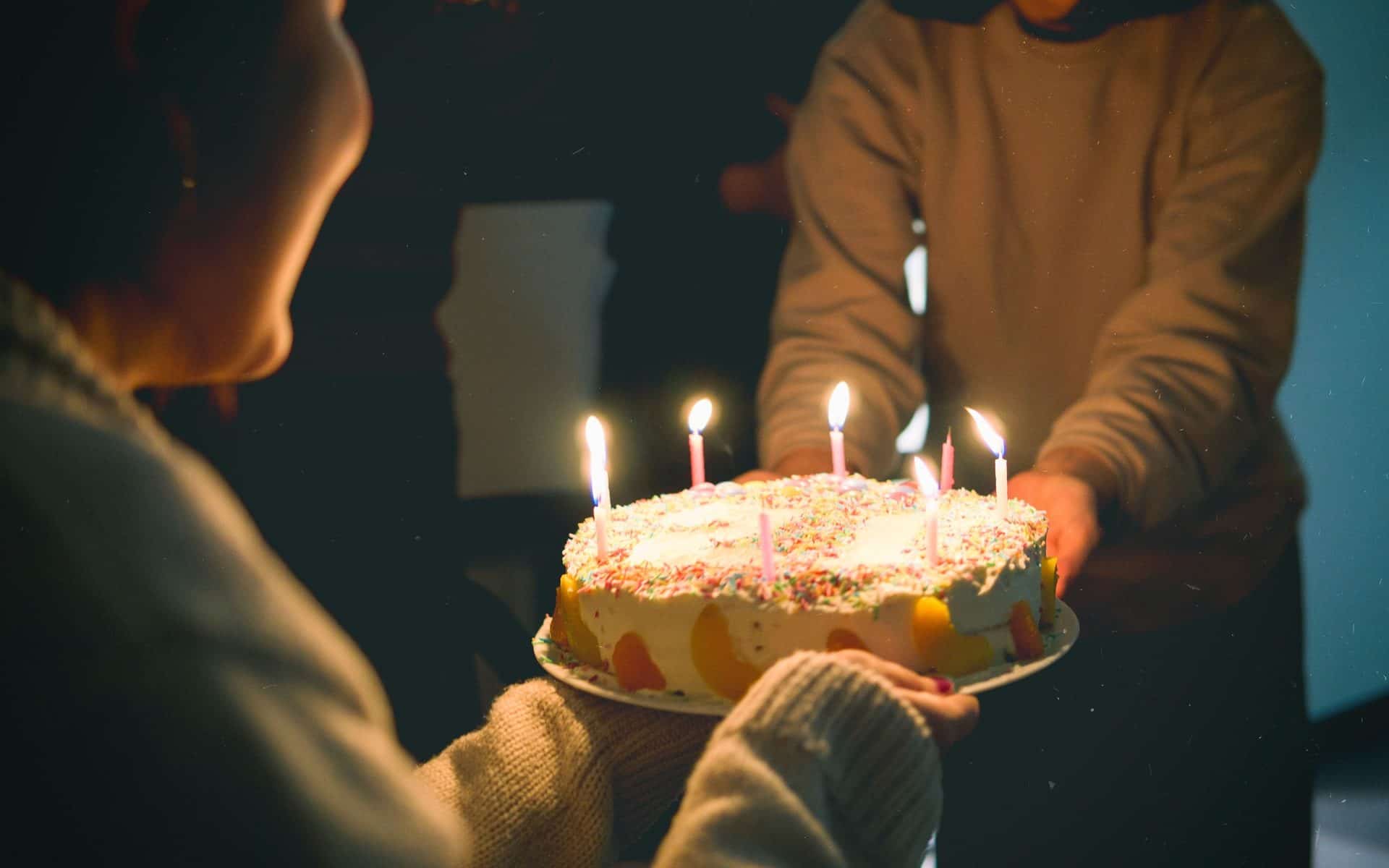 Duas pessoas segurando um bolo de aniversário repleto de velas.