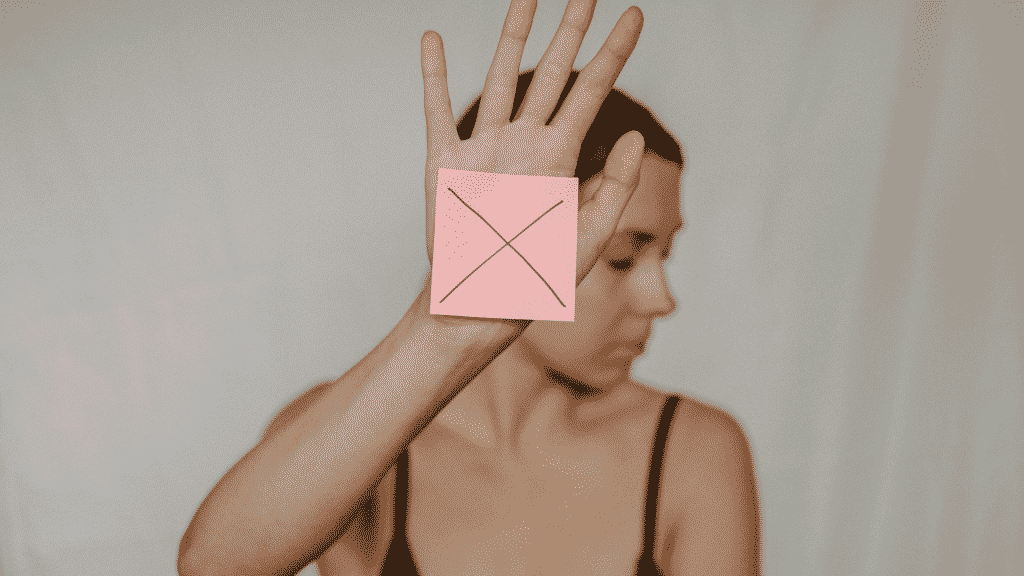 Mulher com o rosto virado para o lado mostrando um papel com a letra X desenhada, na palma de sua mão