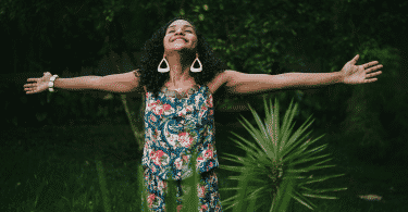 Mulher de braços abertos e sorrindo em um jardim