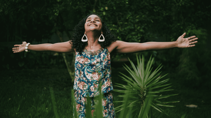 Mulher de braços abertos e sorrindo em um jardim