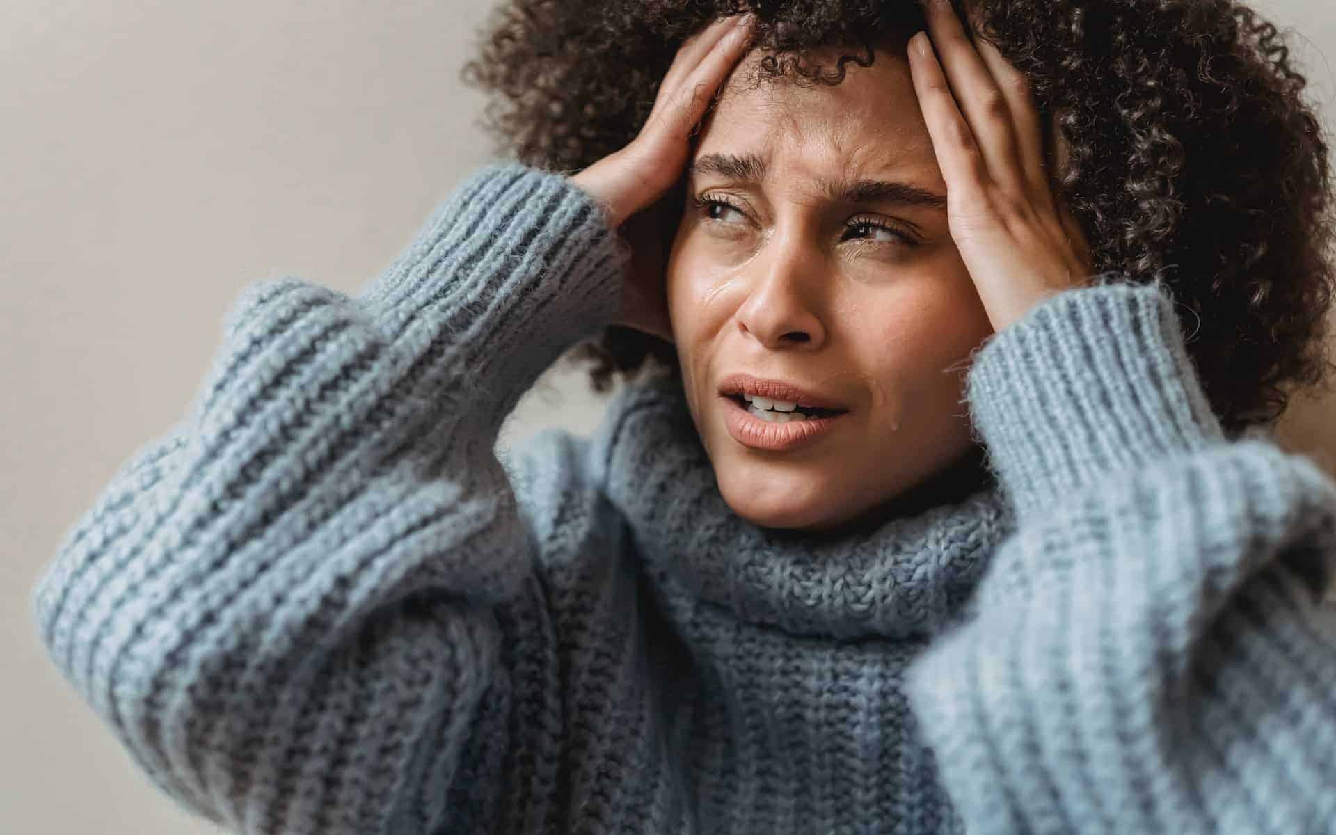 Uma mulher negra chorando. Ela coloca as mãos nas têmporas da sua cabeça.