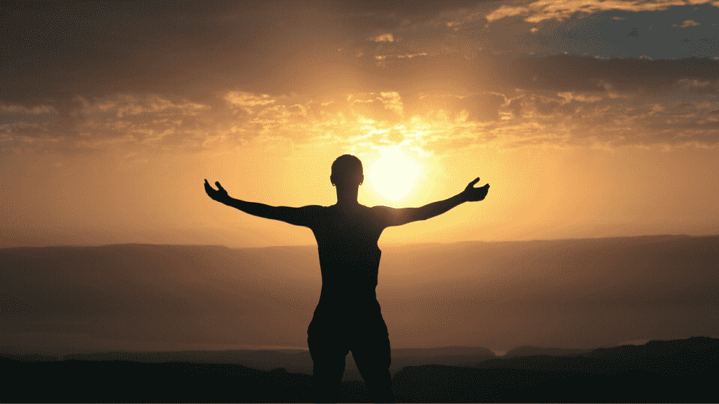 Uma pessoa erguendo seus braços em meio a um pôr do sol.