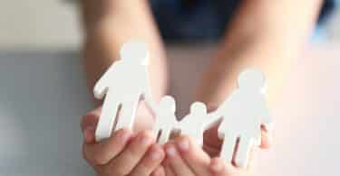 Mãos de uma criança segurando miniaturas de boneco que representam uma família.