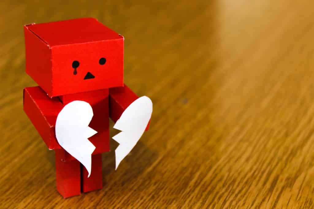 Um robô vermelho de papelão segurando um coração de papel partido.
