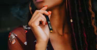 Mulher negra segurando cigarro eletrônico.