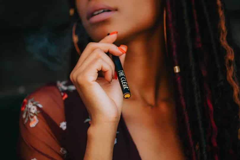 Mulher negra segurando cigarro eletrônico.