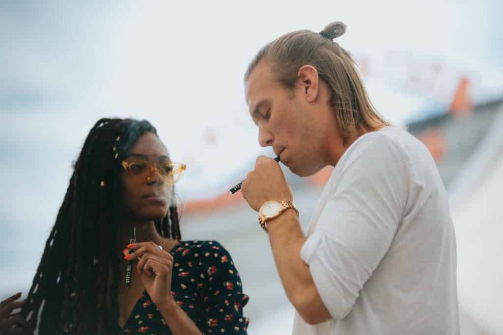 Mulher negra e homem branco usando cigarros eletrônicos.