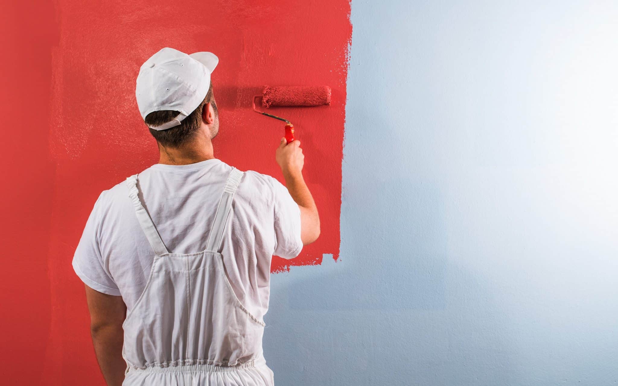 Um homem pintando uma parede com tinta vermelha.
