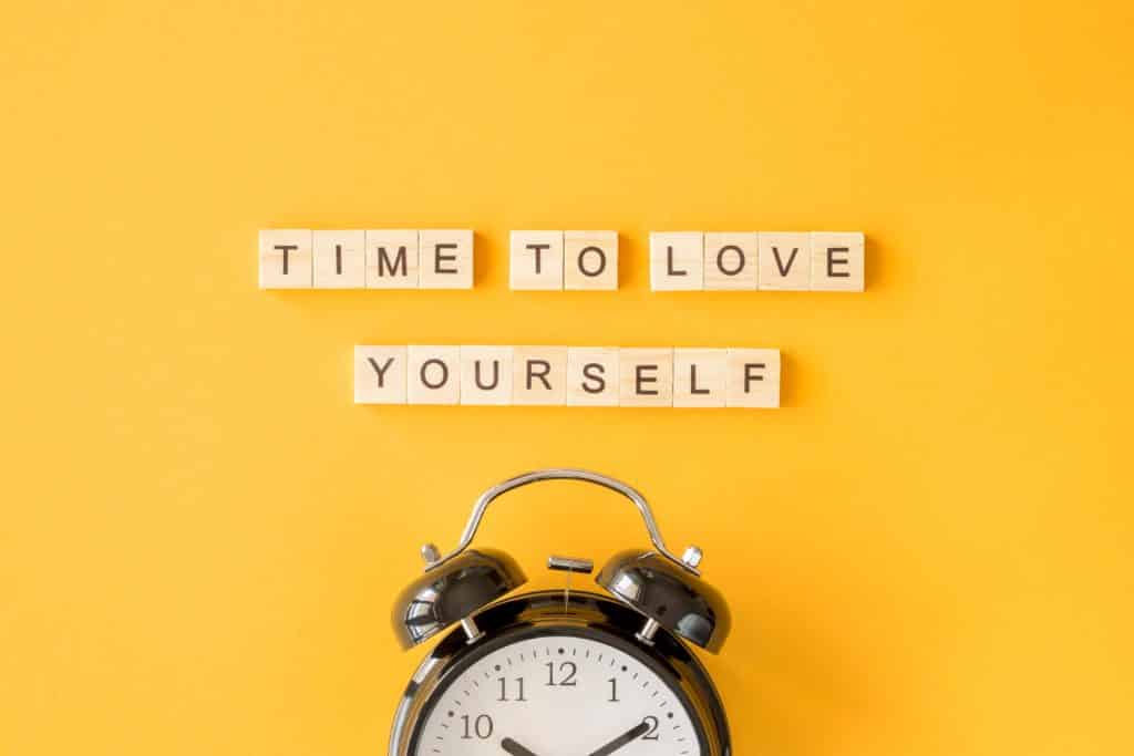 Um despertador. Em cima dele, um letreiro com a frase: "time to love yourself" (trad. tempo de amar a si mesmo)