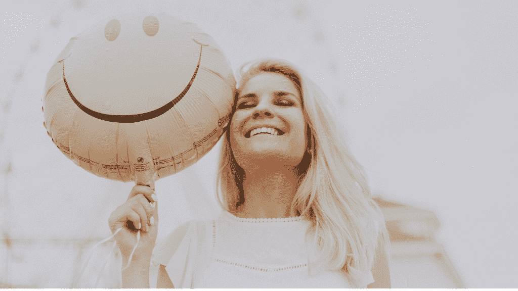 Uma mulher sorrindo. Ela segura um balão de ar que também tem um sorriso desenhado em si.