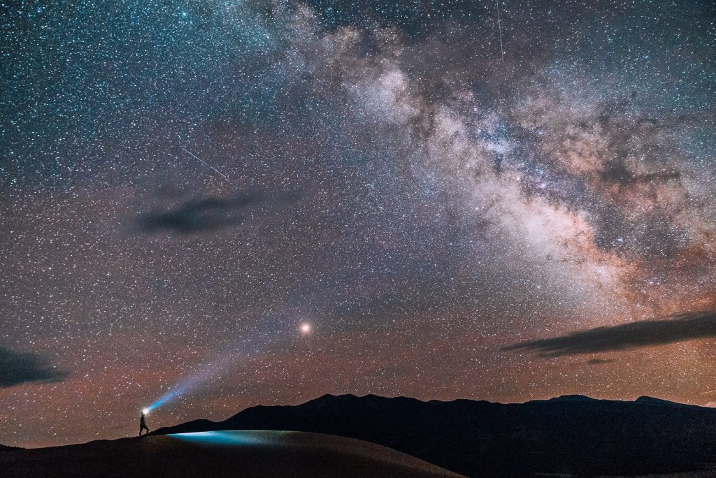 Pessoa segurando lanterna para cima iluminando céu estrelado.