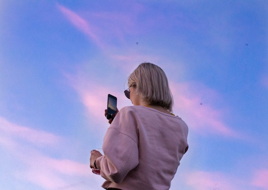 Mulher branca tirando foto do céu.