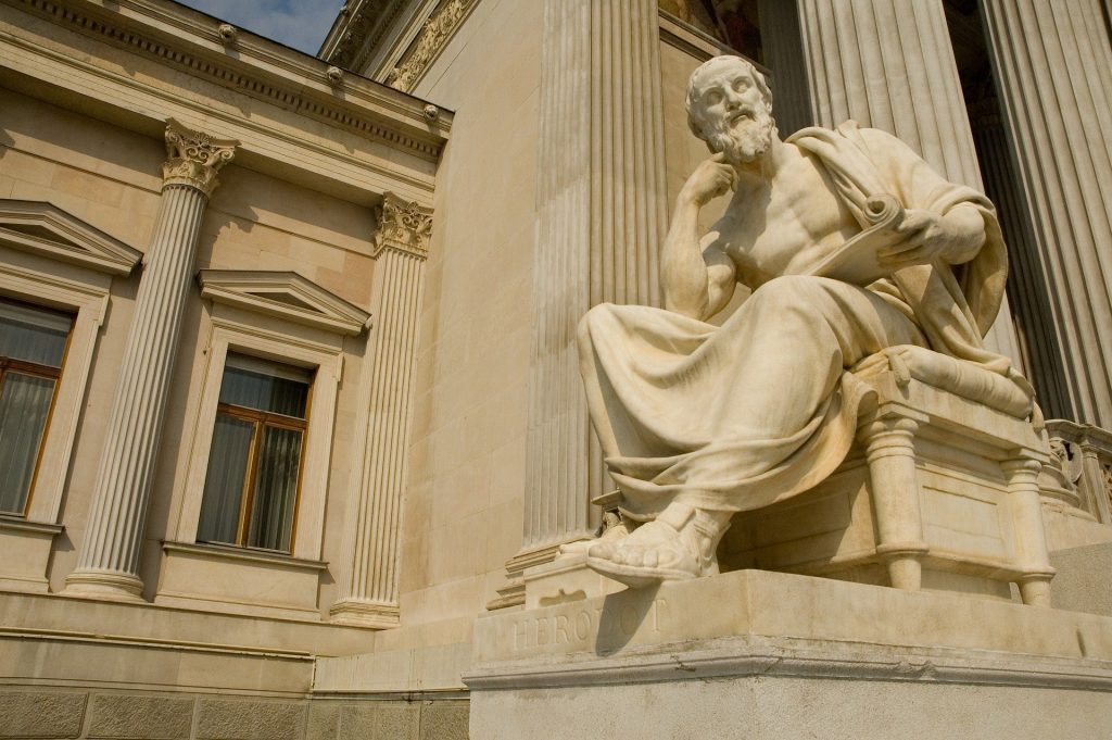 Uma estátua do filósofo e historiador Heródoto. Ele parece contemplar algo.