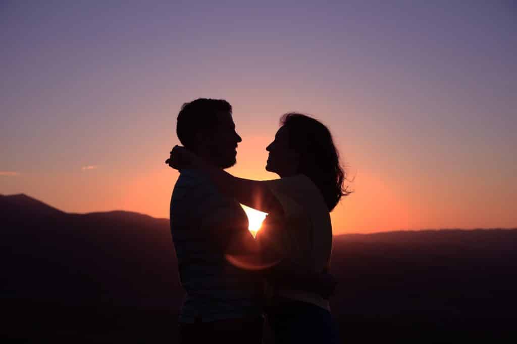Homem e mulher abraçados num pôr do sol.
