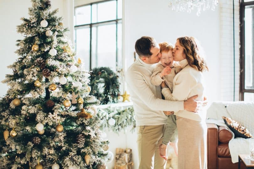 Mulher e homem brancos beijando bochecha de criança.