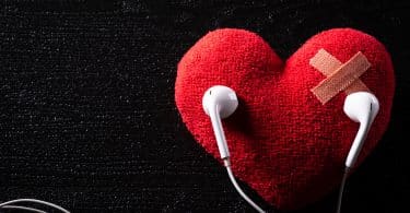 Um coração de pelúcia com um curativo. Sobre o coração, dois fones de ouvidos.