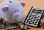 Cofre de porquinho com moedas ao lado de calculadora