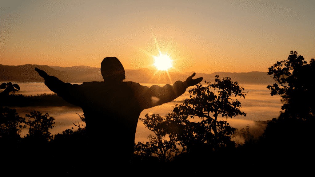 Silhueta de braços abertos observando o por do sol na montanha