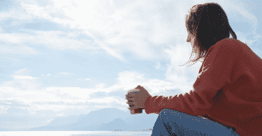 Menina sentada com um copo na mão, observando o mar