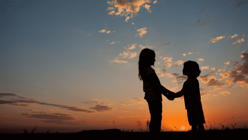 Duas crianças de mãos dadas, se olhando. Ao fundo, o horizonte mostrando o pôr do sol