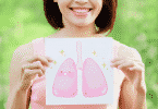 Mulher segurando em frente ao seu peito um desenho de um pulmão. A mulher está sorrindo e há um rosto desenhado no pulmão, também sorrindo