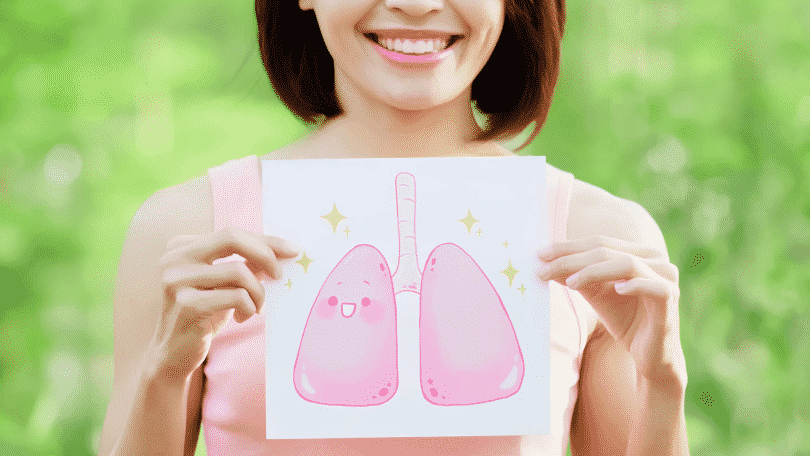 Mulher segurando em frente ao seu peito um desenho de um pulmão. A mulher está sorrindo e há um rosto desenhado no pulmão, também sorrindo