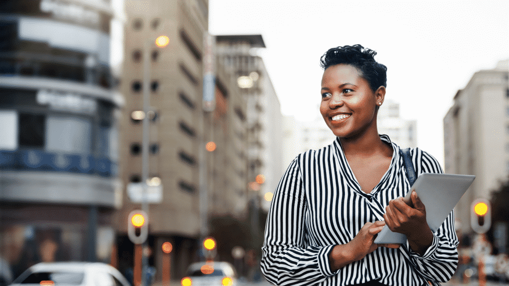 Mulher sorrindo com um tablet na mão, no meio da cidade