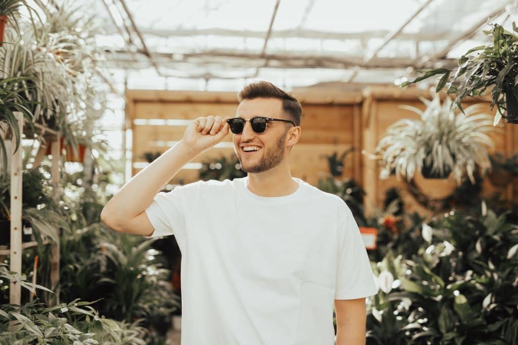 Homem branco no meio de plantas usando óculos escuros.