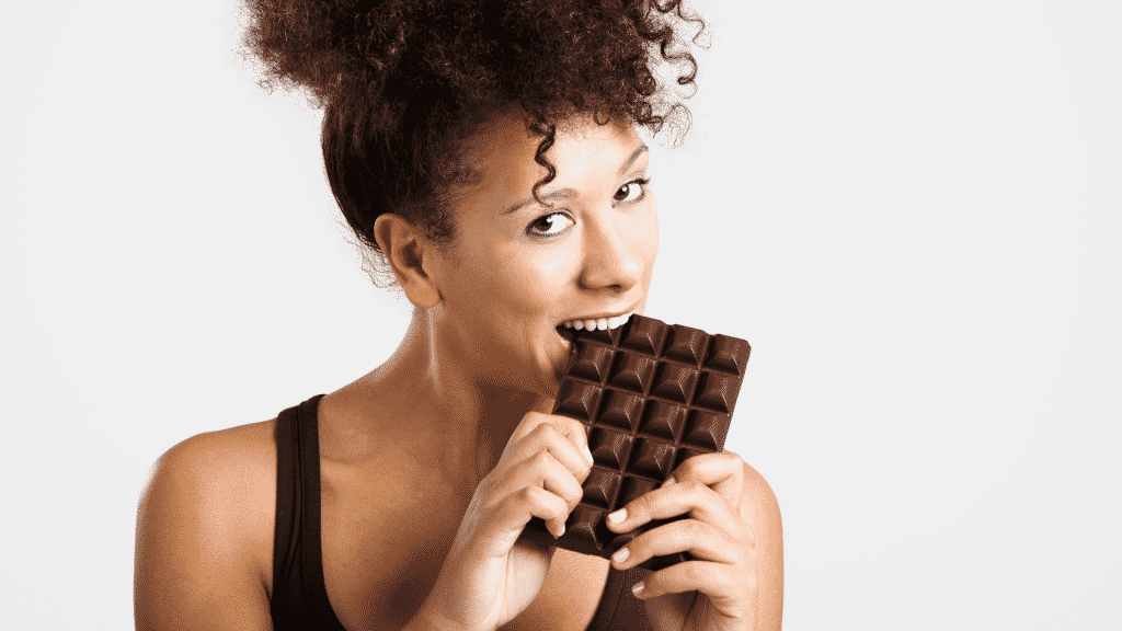 Uma mulher mordendo uma barra de chocolate.