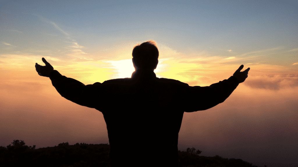 Um homem de braços erguidos situado sob um sol nascente.
