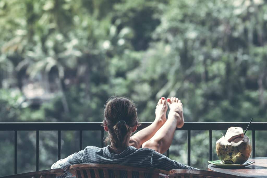 Mulher sentada de frente para várias árvores relaxando com as pernas para o  alto