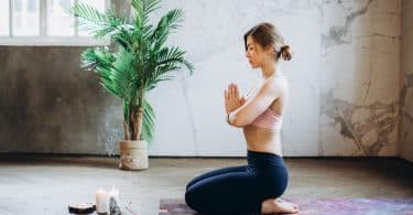 Mulher meditando de joelhos e mãos unidas em uma sala