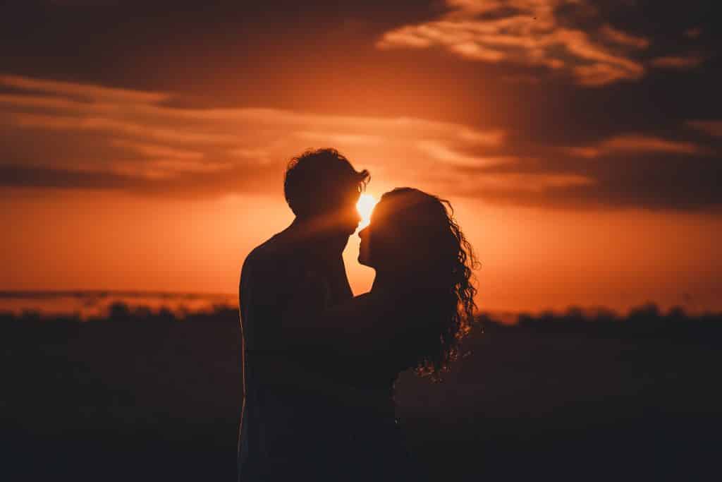 Homem e mulher se abraçando com um pôr do sol atrás