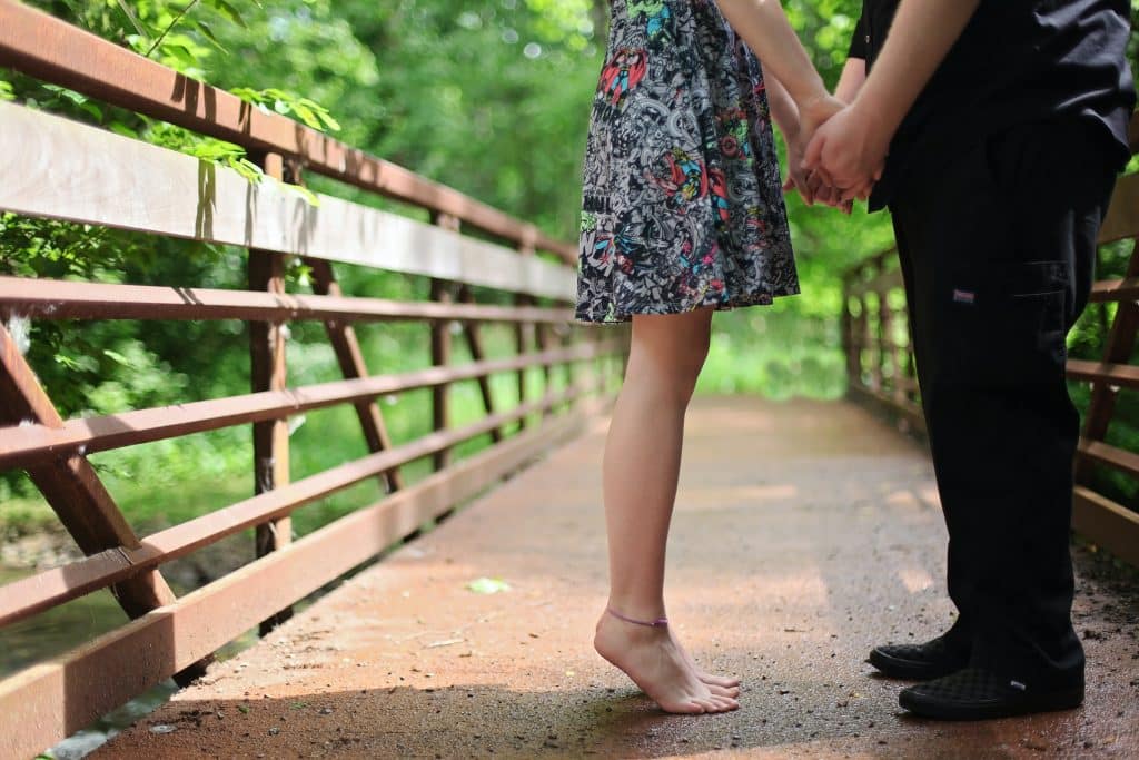 Um casal frente a frente de mãos dadas em uma ponte.