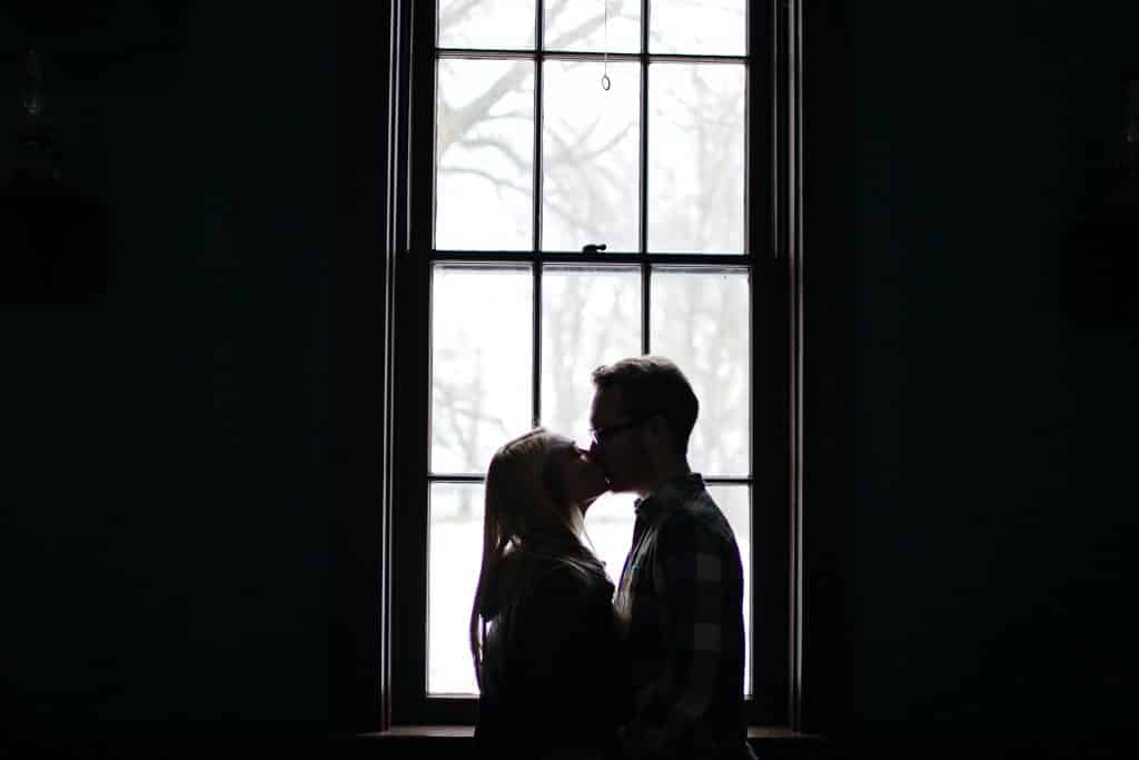 Um casal se beijando em frente a uma janela
