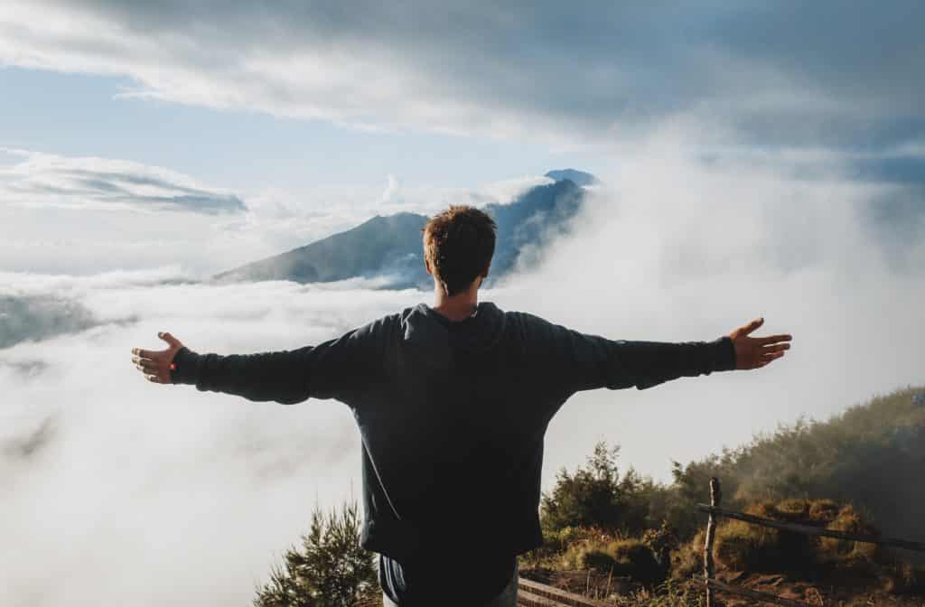 Homem de braços abertos em cima de uma montanha