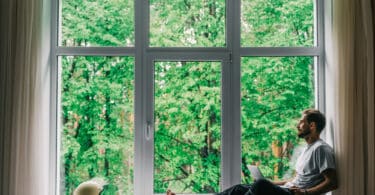 Homem sentado na janela, observando a floresta