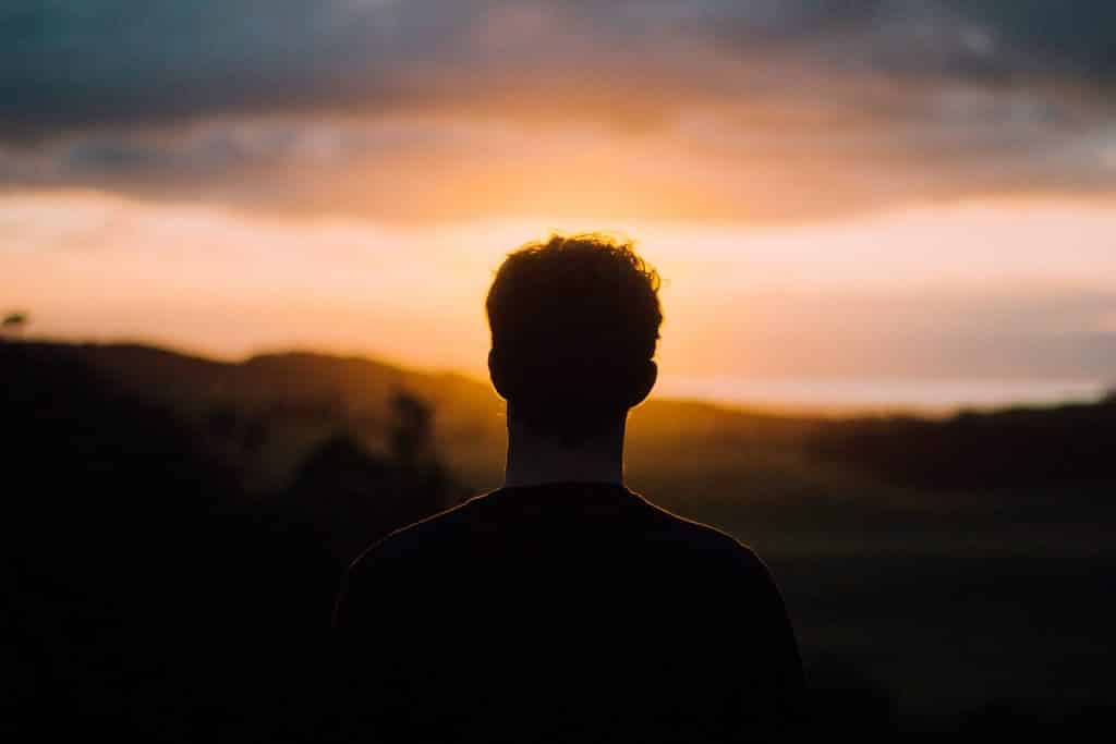 Homem branco de costas no pôr do Sol.