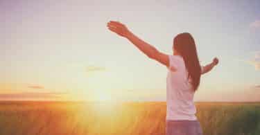 Uma pessoa erguendo e abrindo seus braços em meio a um pôr do sol.
