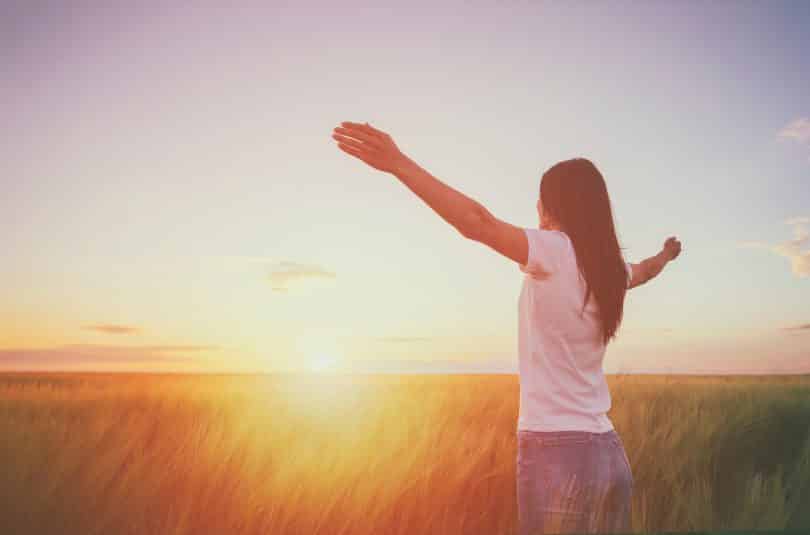 Uma pessoa erguendo e abrindo seus braços em meio a um pôr do sol.