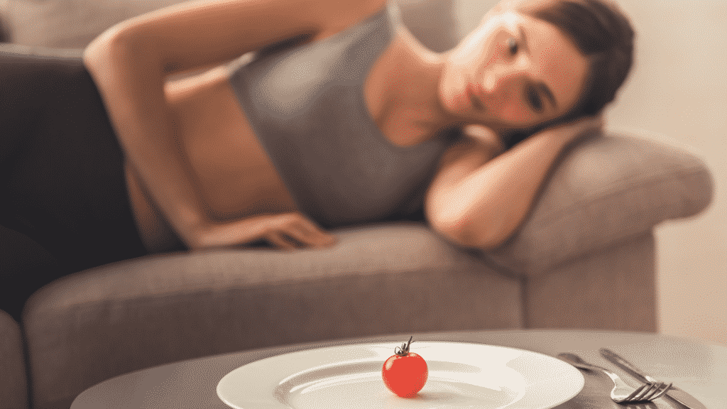 Uma mulher deitada num sofá a observar uma pequena cereja disposta num prato.
