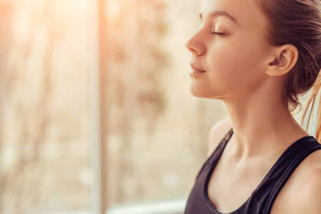Vista lateral de uma jovem mulher com os olhos fechados respirando profundamente enquanto fazia exercícios de respiração
