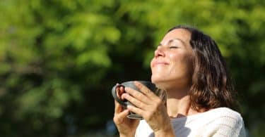 Mulher com um rosto de satisfação. Ela está segurando uma xícara de chá.