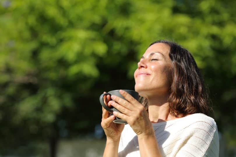 Mulher com um rosto de satisfação. Ela está segurando uma xícara de chá.