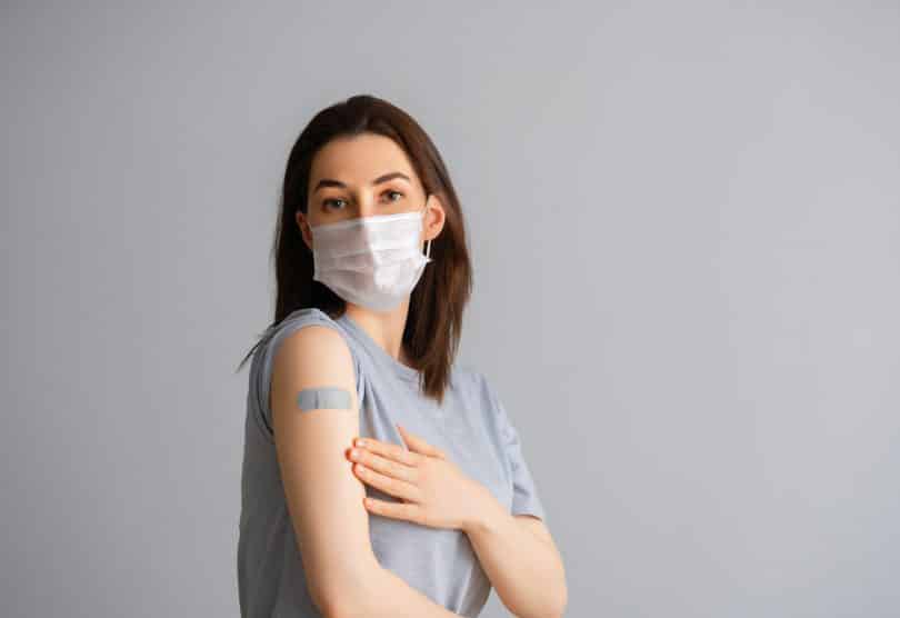 Mulher mostrando o braço com um curativo de vacina.