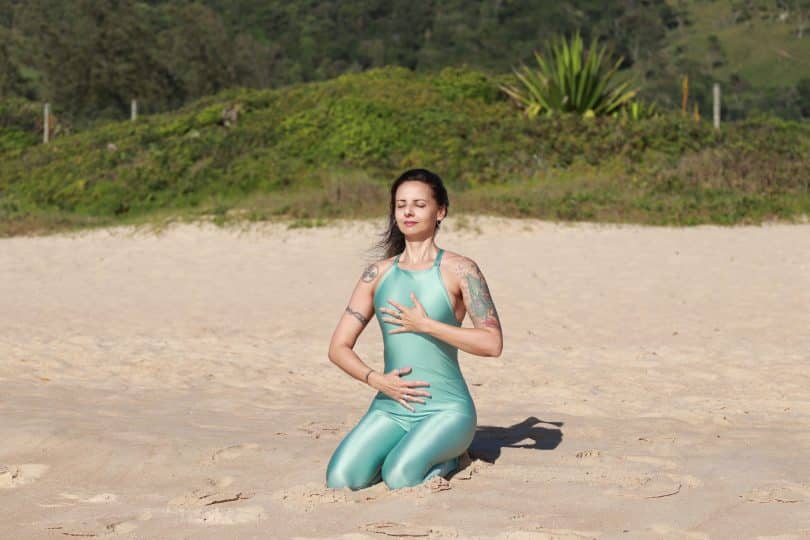 Mulher sentada na praia respirando profundamente.