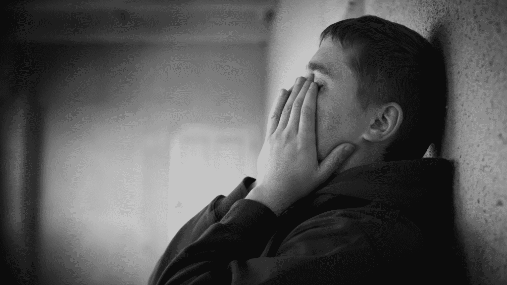 Imagem em preto e branco de um homem com as mãos no rosto, em sinal de tristeza