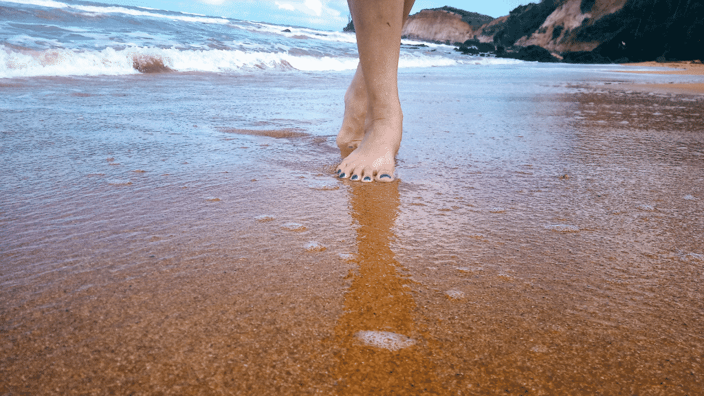 Pessoa com os pés na areia e as águas do mar ao fundo