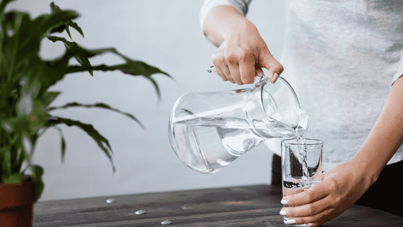 Pessoa colocando água de uma jarra em um copo d'água