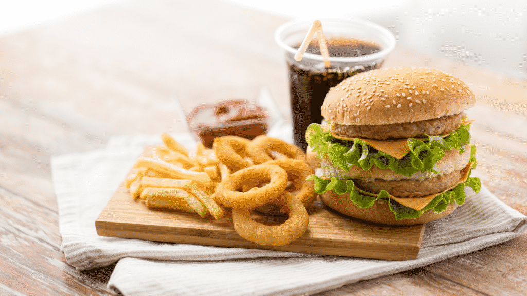 Imagem de um lanche com hambúrguer, batata frita, anéis de cebola, refrigerante e ketchup